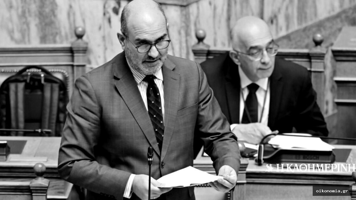 Άνδρας με κοστούμι διαβάζει έγγραφα σε συνεδρίαση κοινοβουλευτικής επιτροπής