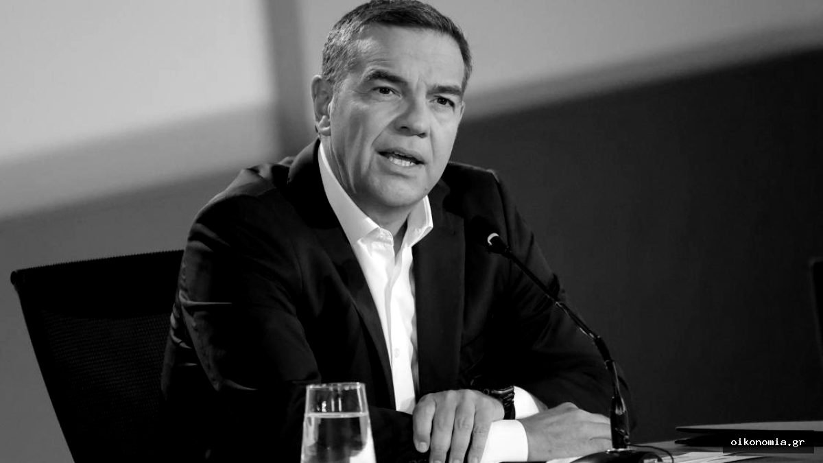 Ο Αλέξης Τσίπρας κάθεται σε τραπέζι με μικρόφωνο μπροστά του.