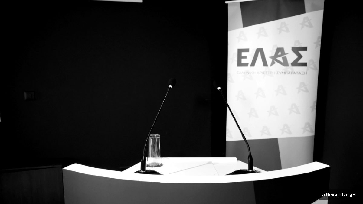 Βήμα με δύο μικρόφωνα και banner της ΕΛ.ΑΣ. σε εσωτερικό χώρο