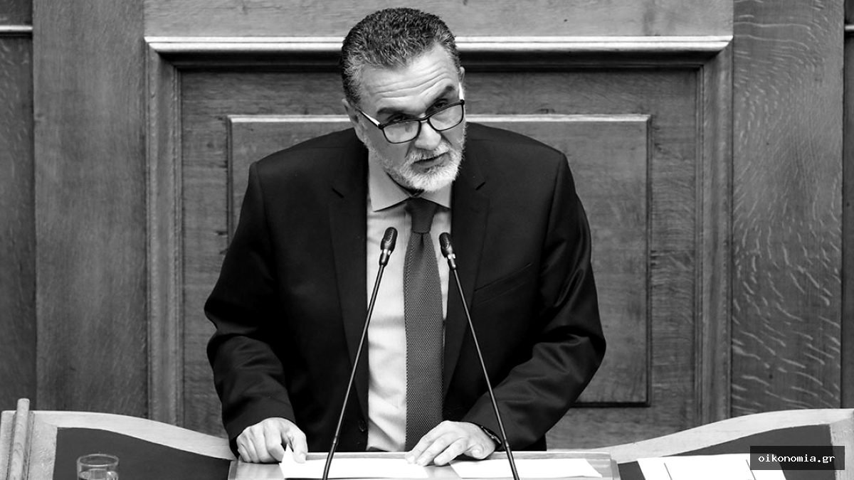 Ο Ιωάννης Τσίμαρης μιλά στο βήμα της Βουλής, μπροστά σε ξύλινη επένδυση.