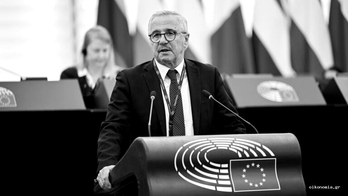 Ο Γιάννης Μανιάτης μιλά από το βήμα του Ευρωπαϊκού Κοινοβουλίου, με σημαίες στο φόντο.