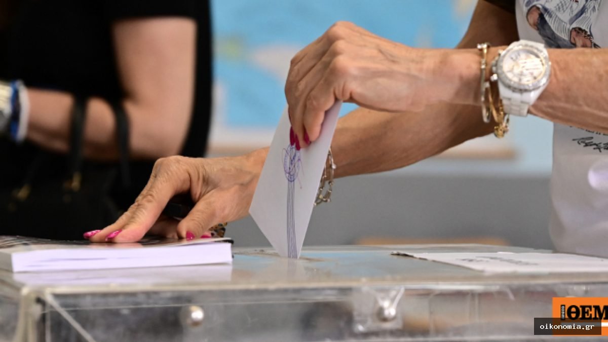 Χέρι ρίχνει ψηφοδέλτιο σε διαφανή κάλπη, με άλλα ψηφοδέλτια τοποθετημένα δίπλα.